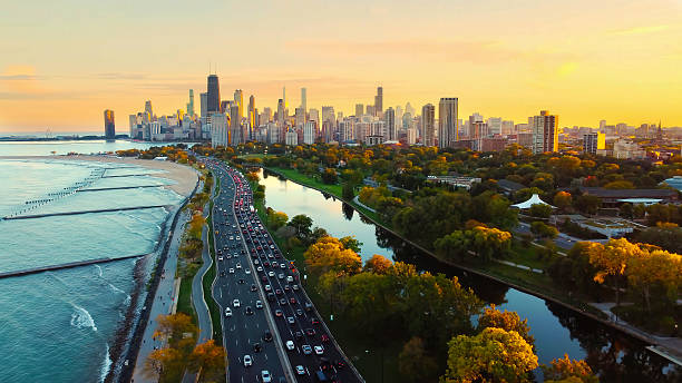 Chicago Cityscape at Sunset with Lakefront View. Aerial view of Chicago skyline at sunset, showing Lake Michigan shoreline, tree-lined parks, and a busy roadway along the waterfront